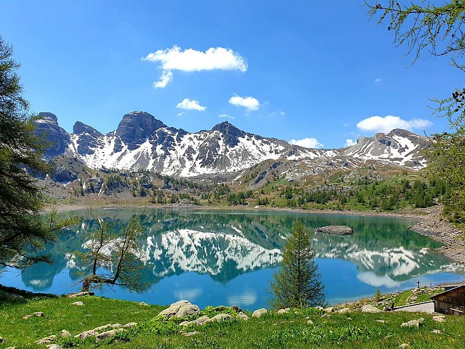 Lake Allos in late spring, with lush green vegetation around the lake and the mountains known as the ‘Têtes du Lac’ in the background, still covered in snow