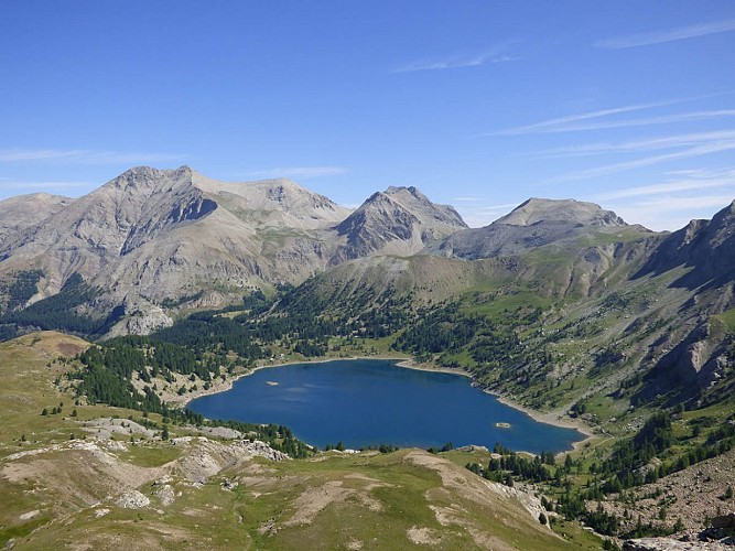 A view of Lake Allos from the Col de l'Encombrette: a large blue lake surrounded by coniferous forests and mountains