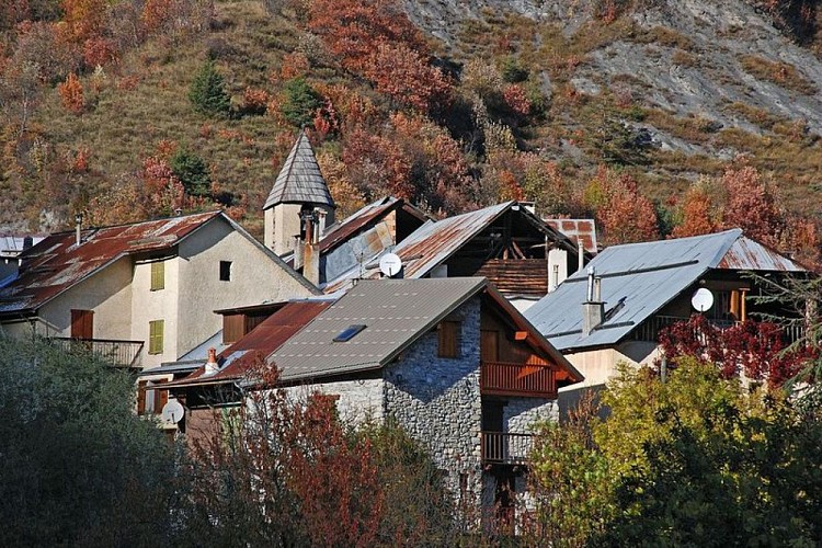 Emergeant de la végétation, les toits et le clocher typique du village d'Entraunes, au mois d'octobre.