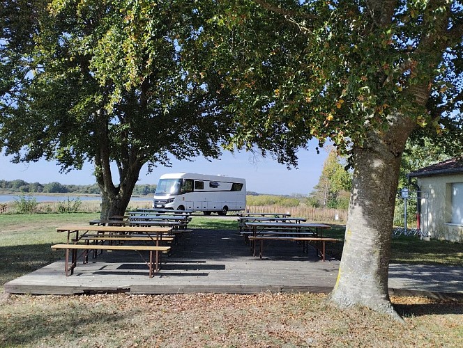 Terrasse à l'ombre du pavillon et emplacements des camping-cars au bord de l'étang, sur la digue.