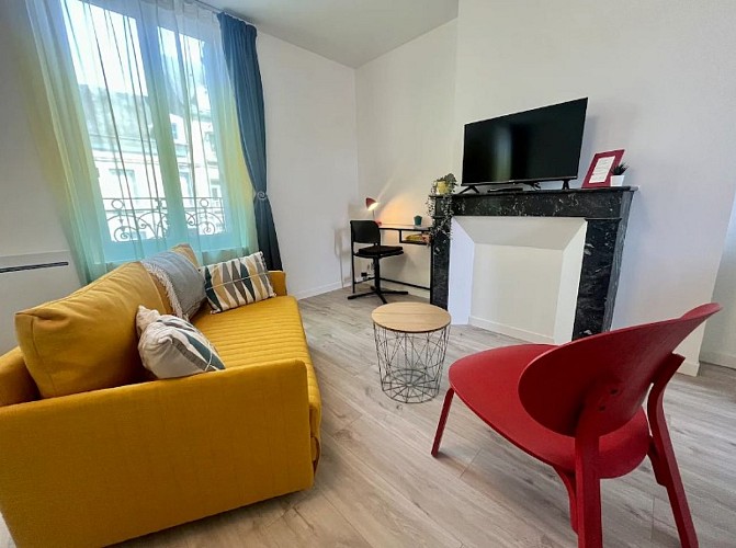 Salon avec canapé jaune, fauteuil rouge, table basse, télévision et bureau