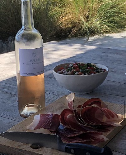 Planche avec tranches de jambon cru, servie avec une assiette de crudités et une bouteille de vin rosé